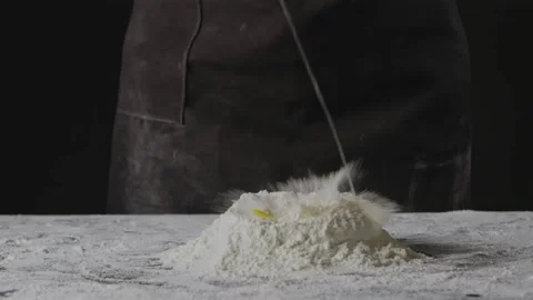 Falling egg into pile of flour on a black background. Process of preparing dough Stock Footage 131443684