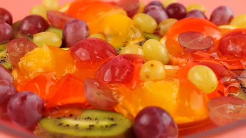 Falling grapes on a multi-colored berry gelatin jelly with orange and kiwi slice Stock Footage 219969980