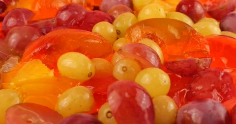 Falling grapes on a multi-colored berry gelatin jelly with orange and kiwi slice Stock-Footage 220125415