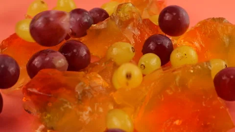 Falling grapes on a multi-colored gelatin jelly on a pink background.  Stock Footage 219969586