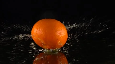 Falling mandarin hitting orange juice surface slow motion shot. Black background Stock Footage 61134653