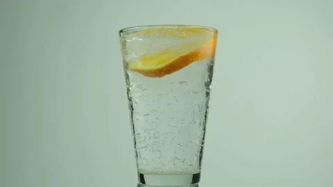Falling of orange slice into a glass of sparkling water with a splash Stock Footage 153431907