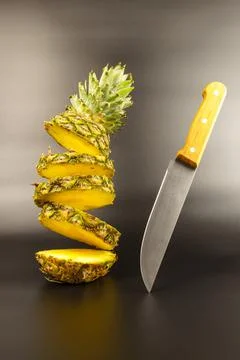 Falling pineapple halves, a knife stands next to it, on a black background. Stock Photos