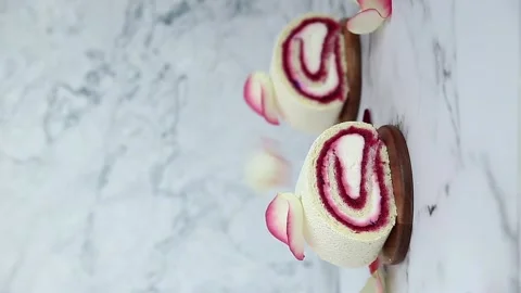 Falling rose petals over raspberry roll cake Stock Footage 148536424