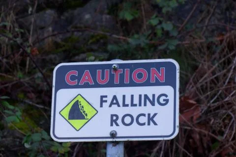 Falling stone warning traffic sign on the road with bushes in the background. Stock Photos