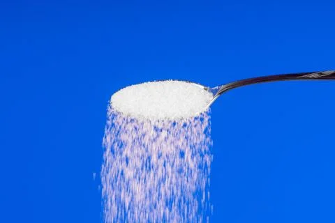 Falling sugar from a spoon on a blue background Stock Photos