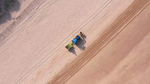 Falling Tracking Shot of a Tractor &amp; Trailer Cleaning a Sandy Beach in 動画素材 113048271