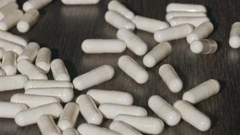 Falling white capsules on a dark table Stock Footage 288986311
