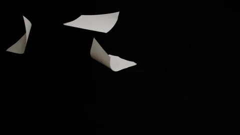 Falling white papers on black background in slow motion Stock Footage