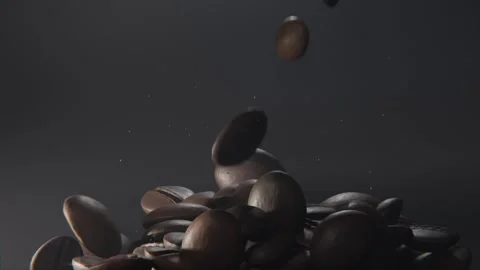 Falling whole roasted coffee beans building pile on dark gray backdrop, dust 스톡 동영상 337505087