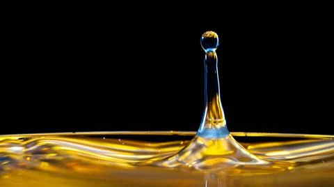 Falling yellow drop on a black background Stock Photos