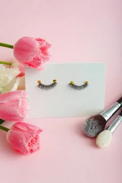 False eyelashes makeup brushes and flowers composition on pink background Stock Photos