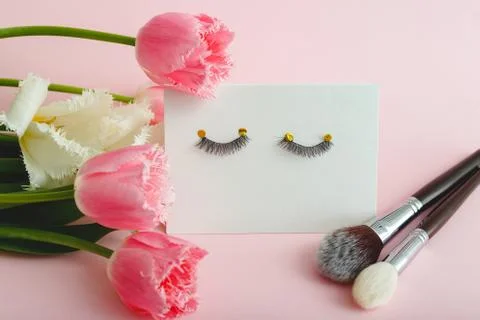 False eyelashes makeup brushes and flowers composition on pink background. Be Stock Photos