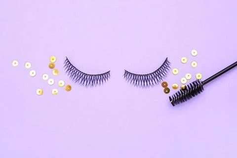 False eyelashes, sequins and mascara brush on violet background, flat lay Stock Photos