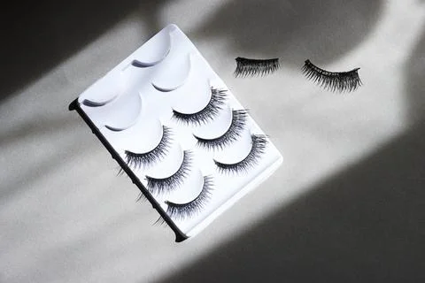 False Eyelashes In White Tray With Loose Lashes On Grey Surface For Beauty Produ Stock Photos