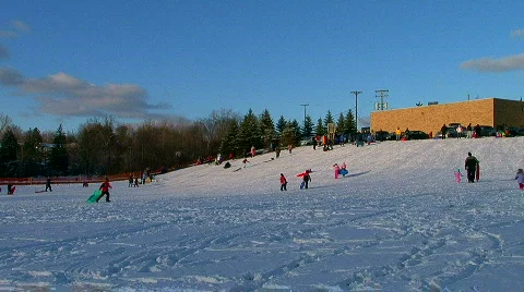 Families and children sledding down hill Stock Footage
