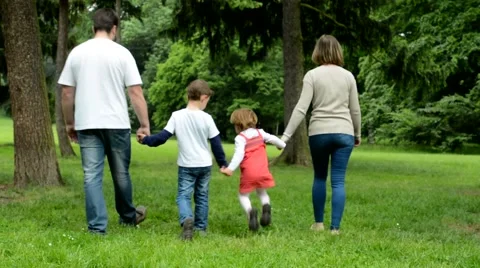 Family (couple in love, girl and boy) walking in park from camera to distance Stock Footage