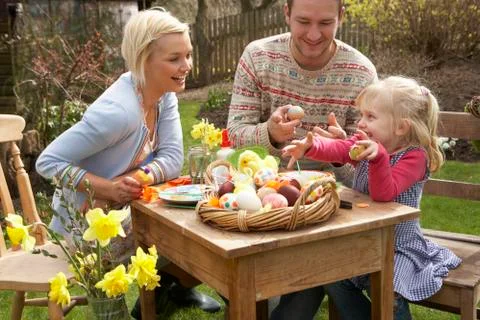 Family decorating easter eggs on table outdoors Foto stock