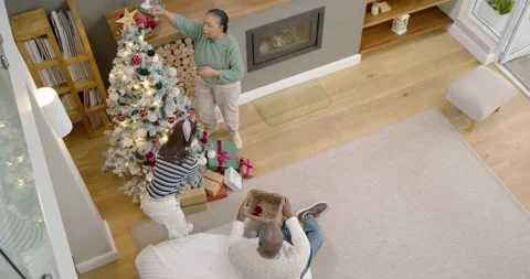 Family decorating flocked tree for Xmas at home, man with basket handing Stock Footage 343545215