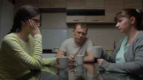 Family discusses problems sitting in the at a table in the kitchen drinking tea Stock Footage 130743390