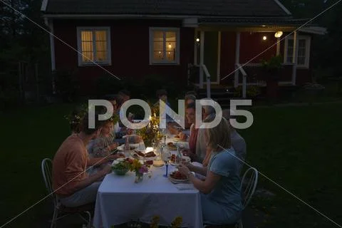 Family enjoying candlelight dinner at patio table outside house at night Stock Photos