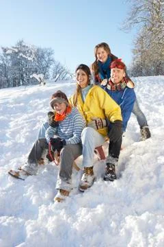 Family enjoying sledging down snowy hill Stock Photos