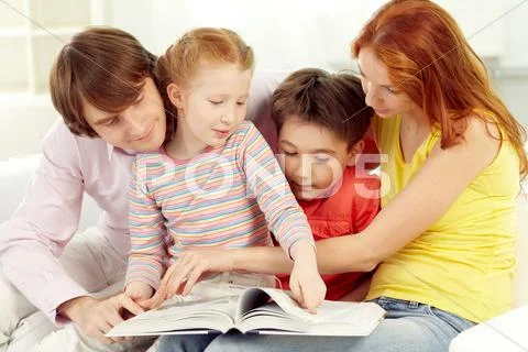Family of four reading book together at home Stock Photos