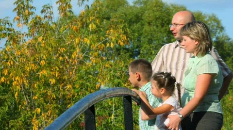 Family of four standing on bridge in park and looks away, profile Stock Footage