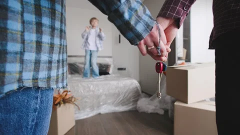 Family holds house keys while son jumps on a bed covered with plastic. Cardboard Stock Footage 346226580