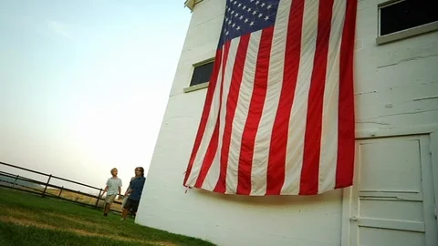 Family looks at large American Flag waving on the side of white barn, Utah. Stock Footage