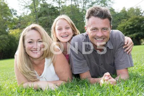 Family lying on grass in park together summertime Stock Photos