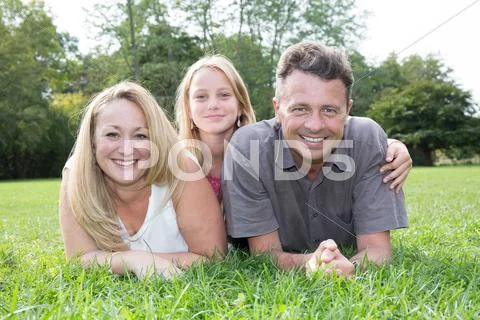 Family lying on grass in park together summertime Stock Photos