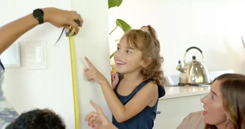 Family measuring height at kitchen wall with man holding yellow tape, marking Stock Footage 336438237