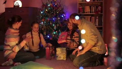 A family is opening their presents while sitting under a christmas tree.  Stock Footage 76254964