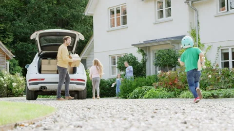 Family Outside New Home On Moving Day Unloading Boxes From Car As Son With Stock Footage