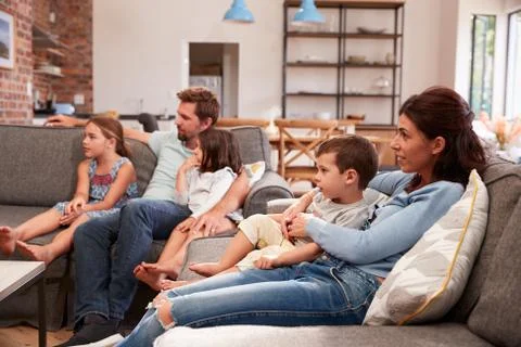Family Sit On Sofa In Open Plan Lounge Watching Television Fotos de archivo