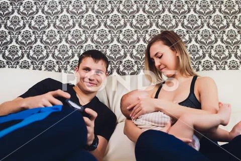Family sits on the couch, a man plays in the console. Stock Photos
