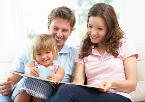 Family Sitting On Sofa Reading Book At Home Stock Photos