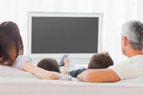 Family sitting on sofa watching television together Stock Photos