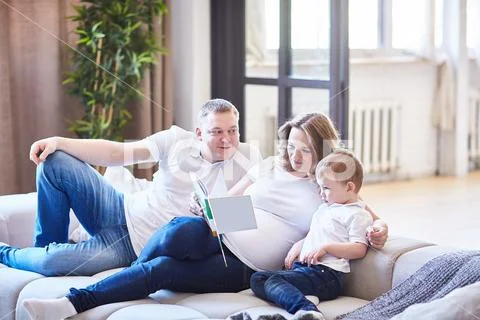 Family with a small child sitting on the couch and reading a book. Stock Photos