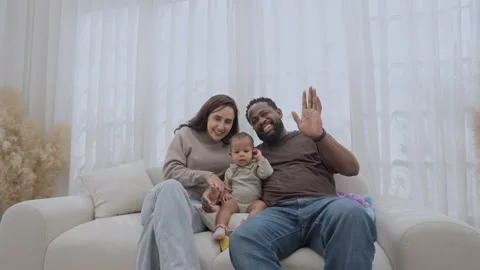 Family smiles and waves while sitting together in a cozy living room Stock Footage 303824380