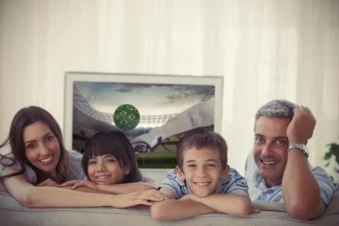 Family smiling at the camera with world cup showing on television Stock Photos