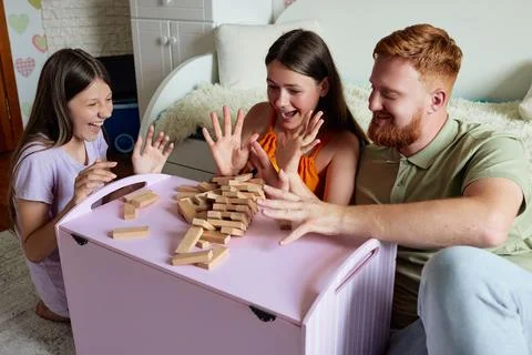 Family of three laughs while playing a game of wooden blocks in a bedroom Foto stock