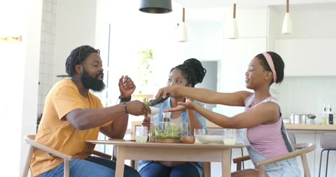 Family of three sitting at dining table, woman passing black tongs, man serving Stock Footage 345064177