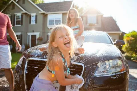 A family washes their car in the driveway of their home on a sunny summer Stock Photos