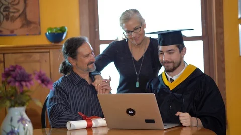 Family watches computer as son, dressed in graduation costume switches sides Stock Footage