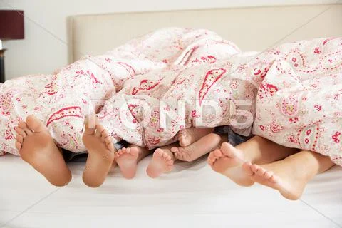 Family's feet poking out from duvet in bed Stock Photos