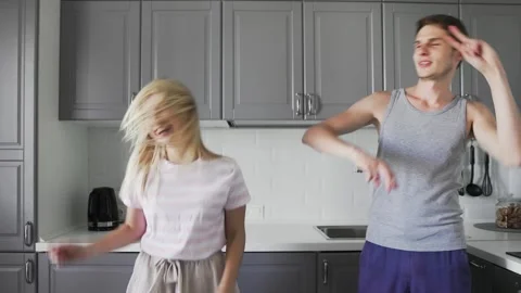 Fancy funny young people smiling, fooling and dancing together in the kitchen at Stock Footage 130384480