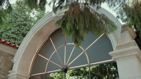Fanlight Arched Window in Stone Facade Framed by Pine Branches and Ivy Stock Footage 343697779