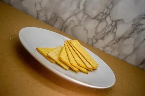A fanned arrangement of golden, rectangular crackers on a crisp white plate.. Foto stock